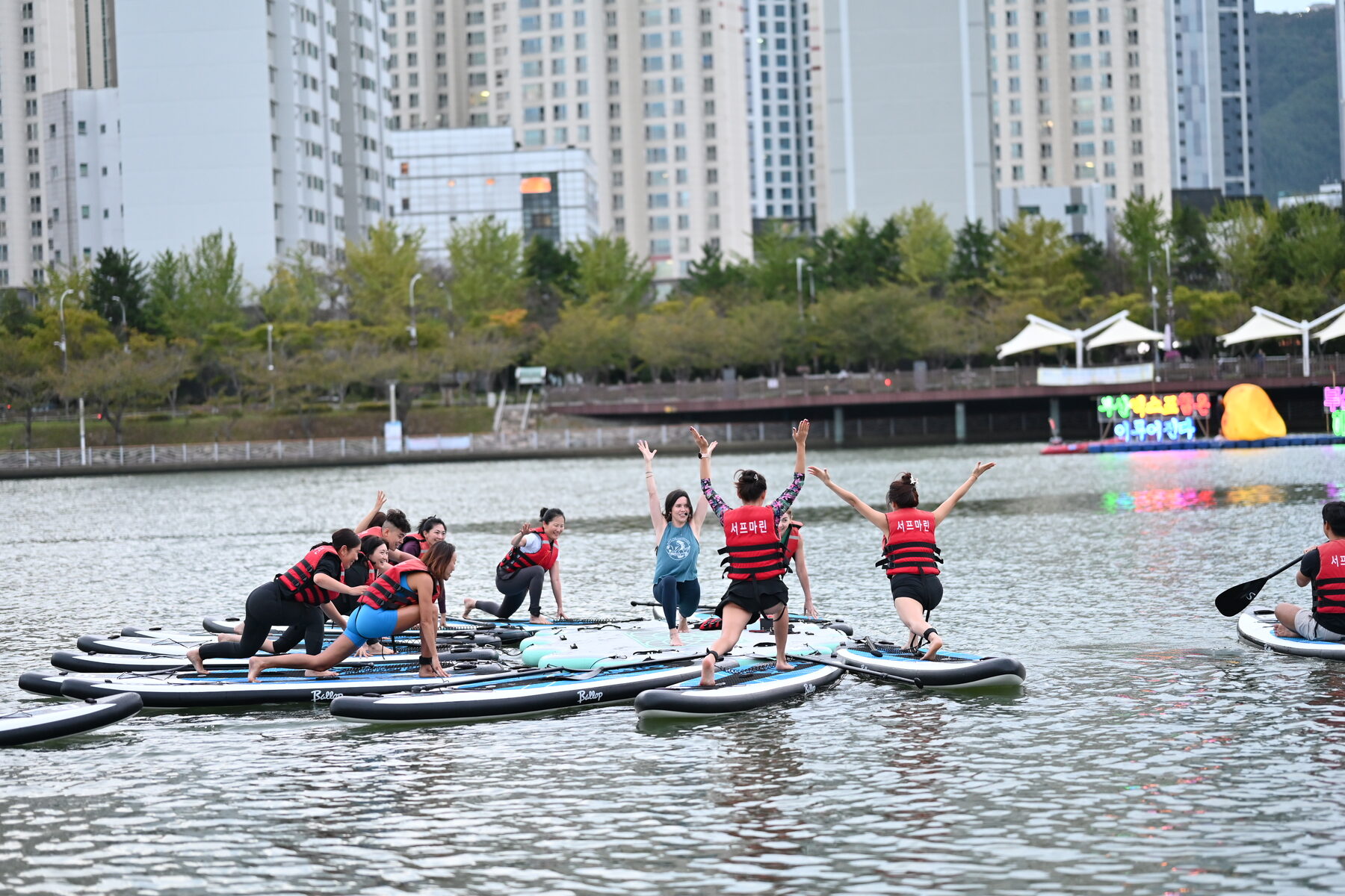 A WellMi group paddleboard yoga class on the water, city skyline behind